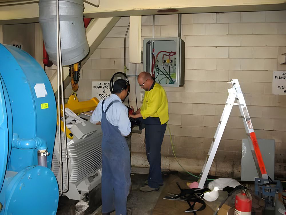 Electrician wiring a control panel beside large blue industrial water tanks.