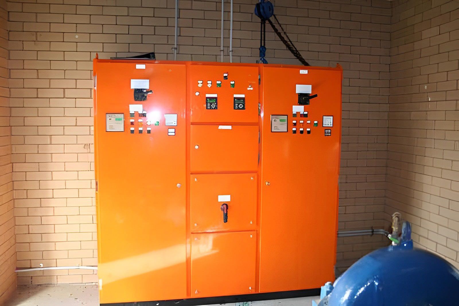 Large orange industrial switchboard installation mounted against a brick wall.
