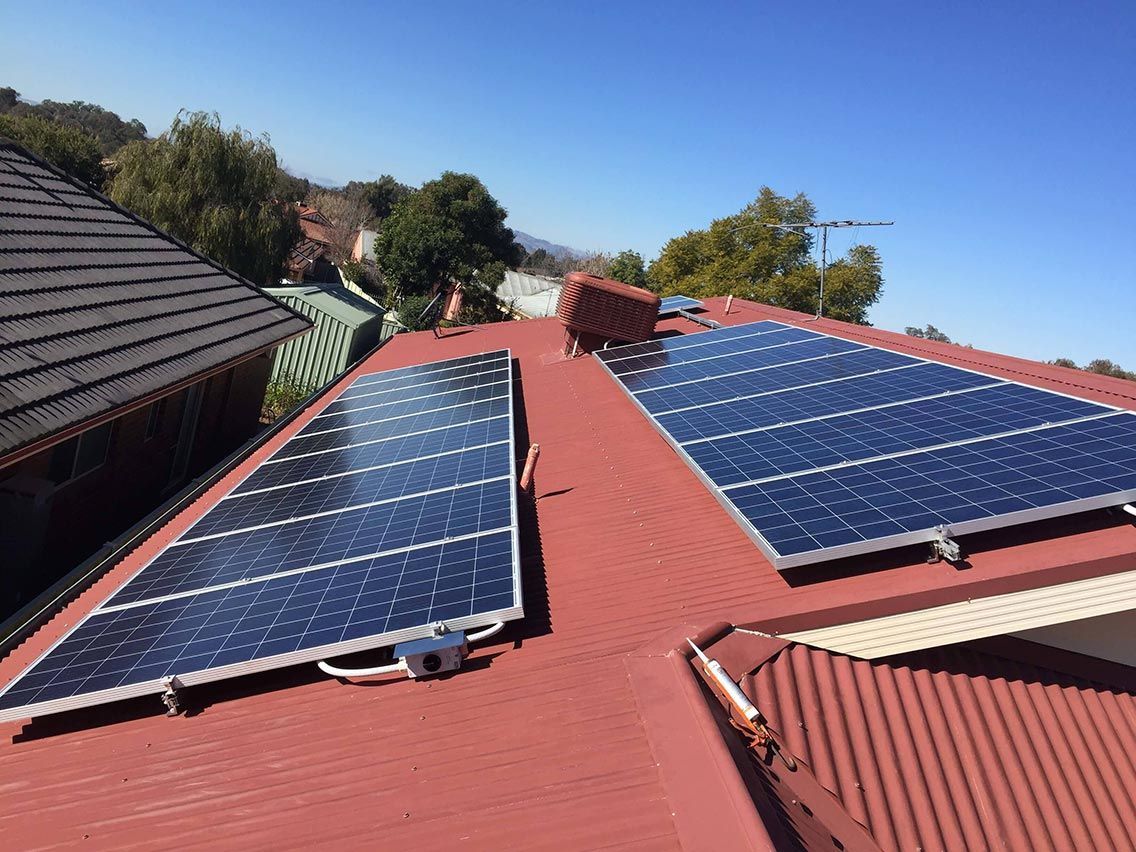 Rooftop solar panel array installed on a red corrugated iron roof.